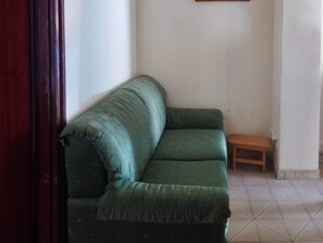 Ein grünes Sofa in einem Raum mit Fliesenboden und einem kleinen Holzschemel.