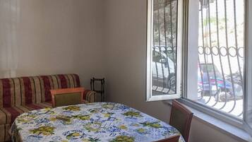 Une pièce comprenant une table à manger, un canapé et une fenêtre donnant sur des voitures garées.