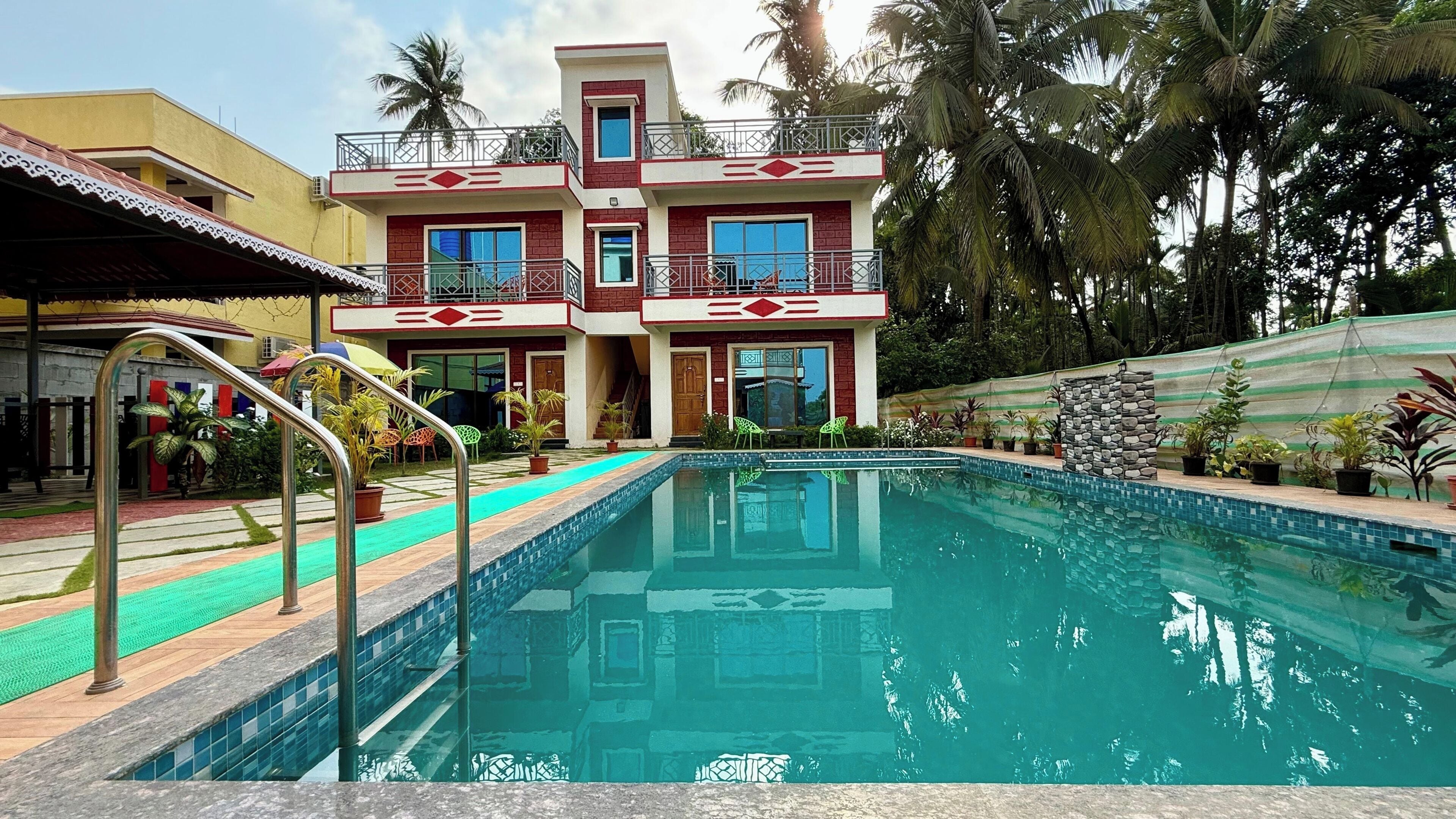 Una piscina con un edificio de dos plantas al fondo, rodeada de vegetación tropical.