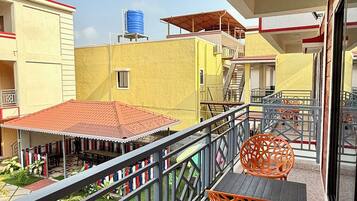 Un balcón con mobiliario exterior, una piscina y vistas a edificios cercanos.