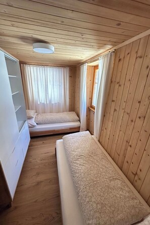 Ein kleines, gemütliches Zimmer mit zwei Betten, einem Fenster mit Vorhängen und einer Deckenleuchte.