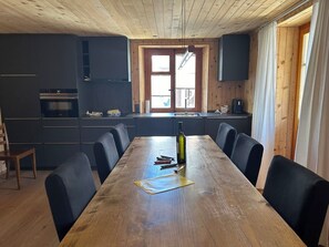 Moderni keittiö, jossa on tummat kaapit, puinen ruokapöytä ja suuri ikkuna.