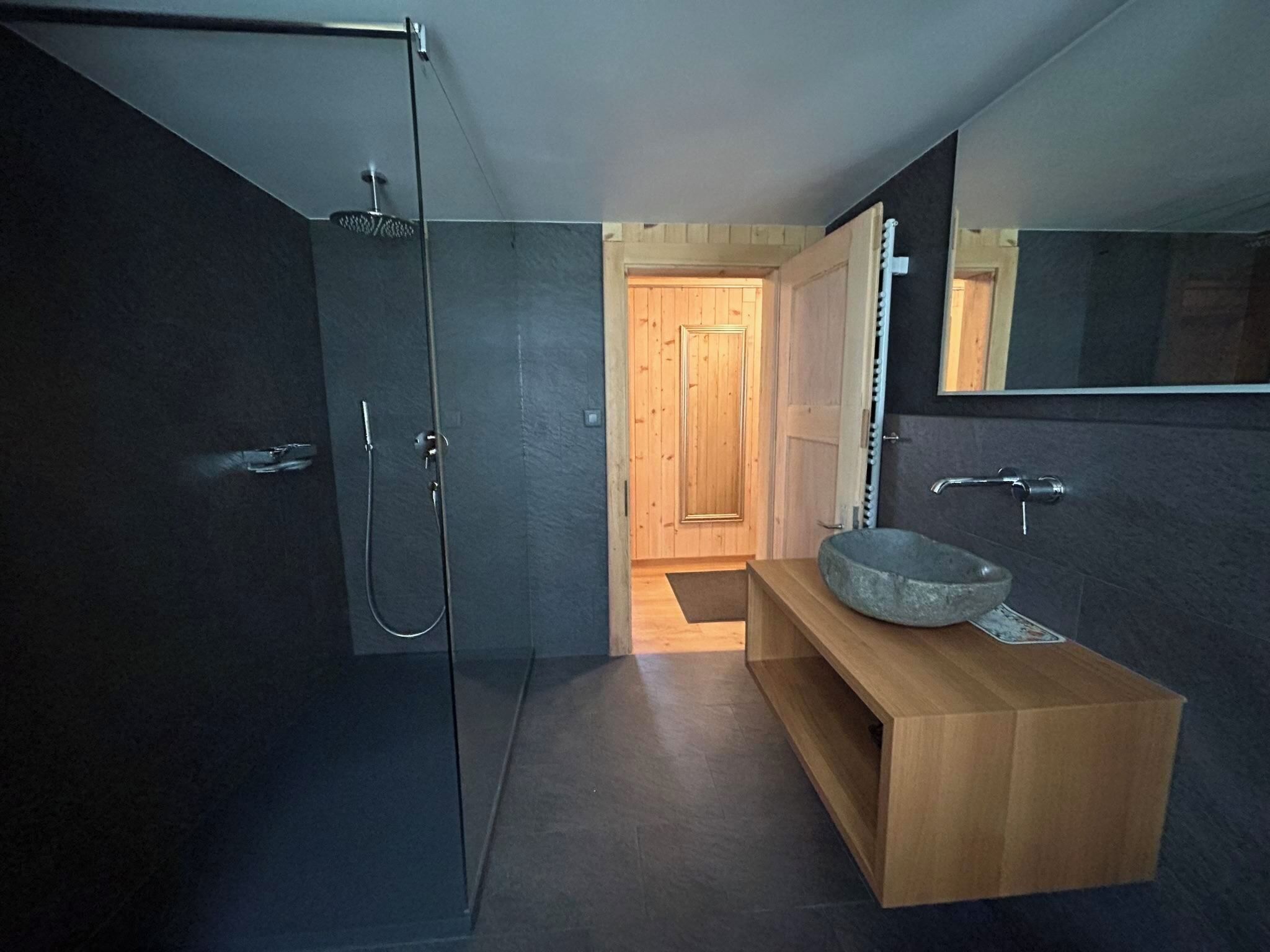 A modern bathroom with a glass shower enclosure, a wooden vanity with a stone basin, and a large mirror.