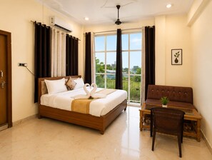 A hotel room with a bed, a sofa, a small table, and a balcony with curtains. - The Yash Hotel And Resort (Faizabad)