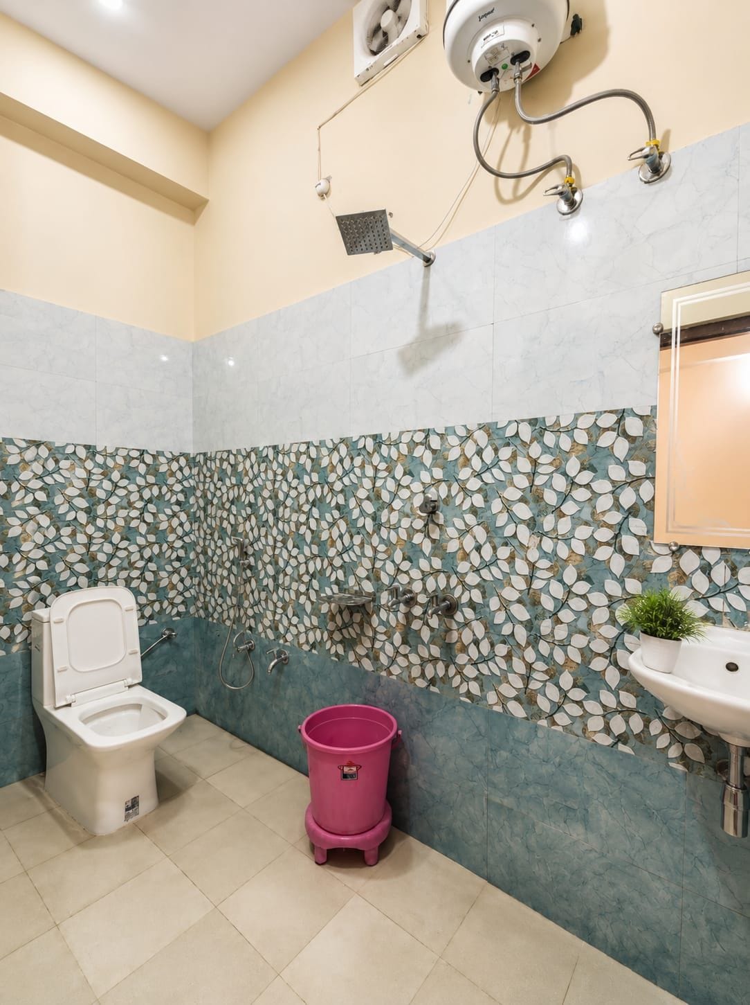 A bathroom with a toilet, a sink, a shower, and a decorative leaf-patterned wall.