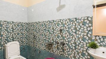 A bathroom with a toilet, a sink, a shower, and a decorative leaf-patterned wall.