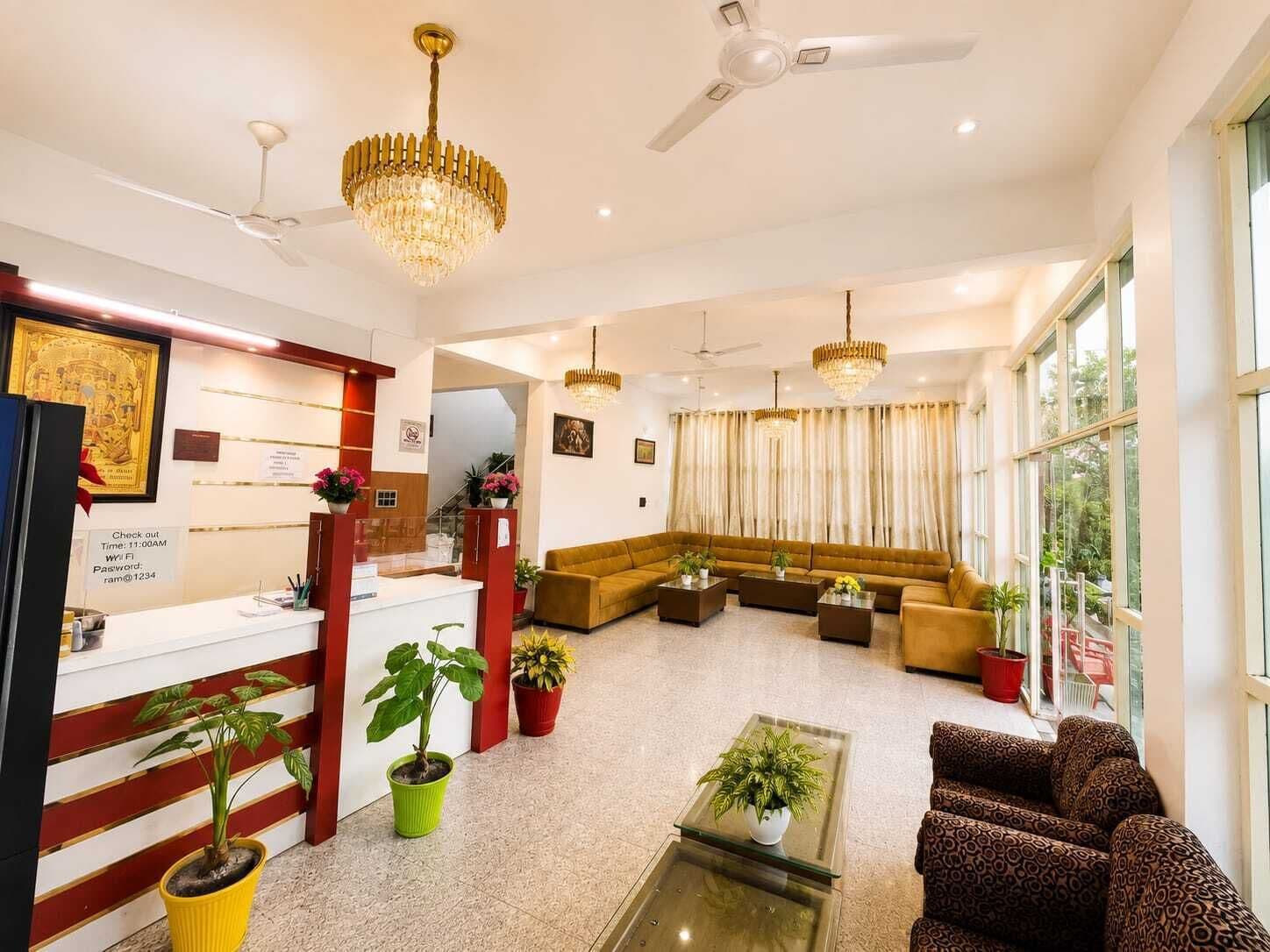 Um hall de hotel com balcão de recepção, área de estar, ventiladores no teto e amplas janelas.
