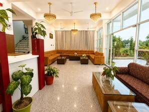A modern living room with a sectional sofa, a glass coffee table, and multiple potted plants. - The Yash Hotel And Resort (Faizabad)