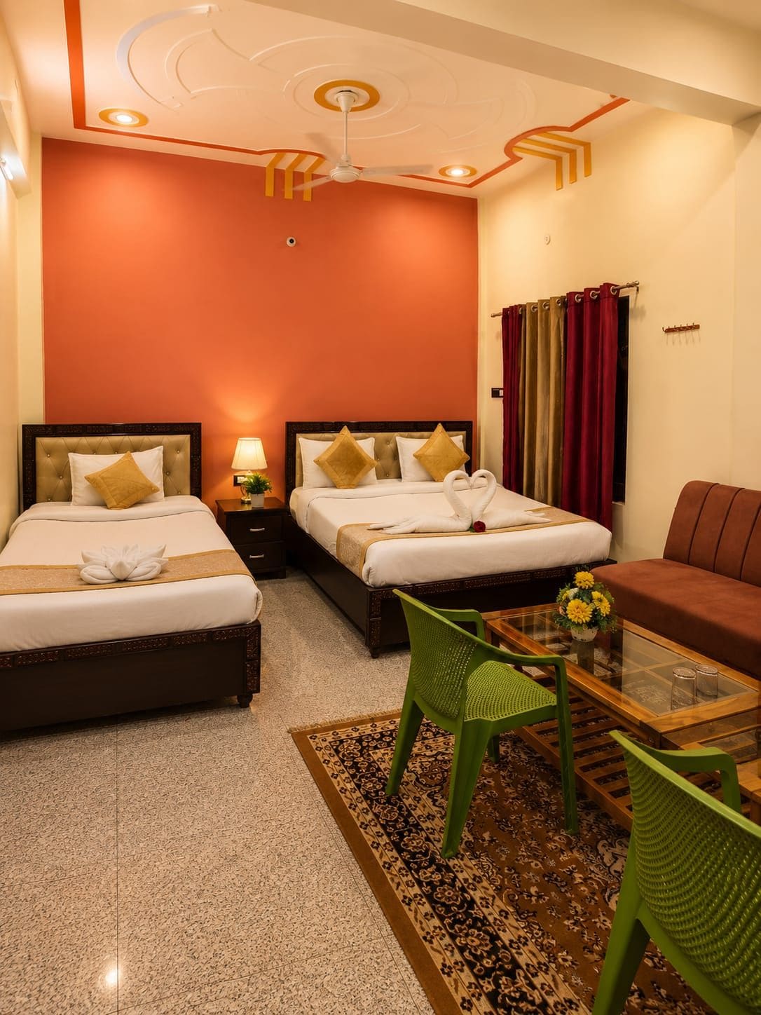 A hotel room with two beds, a green chair, a sofa, a glass coffee table, and a patterned rug.