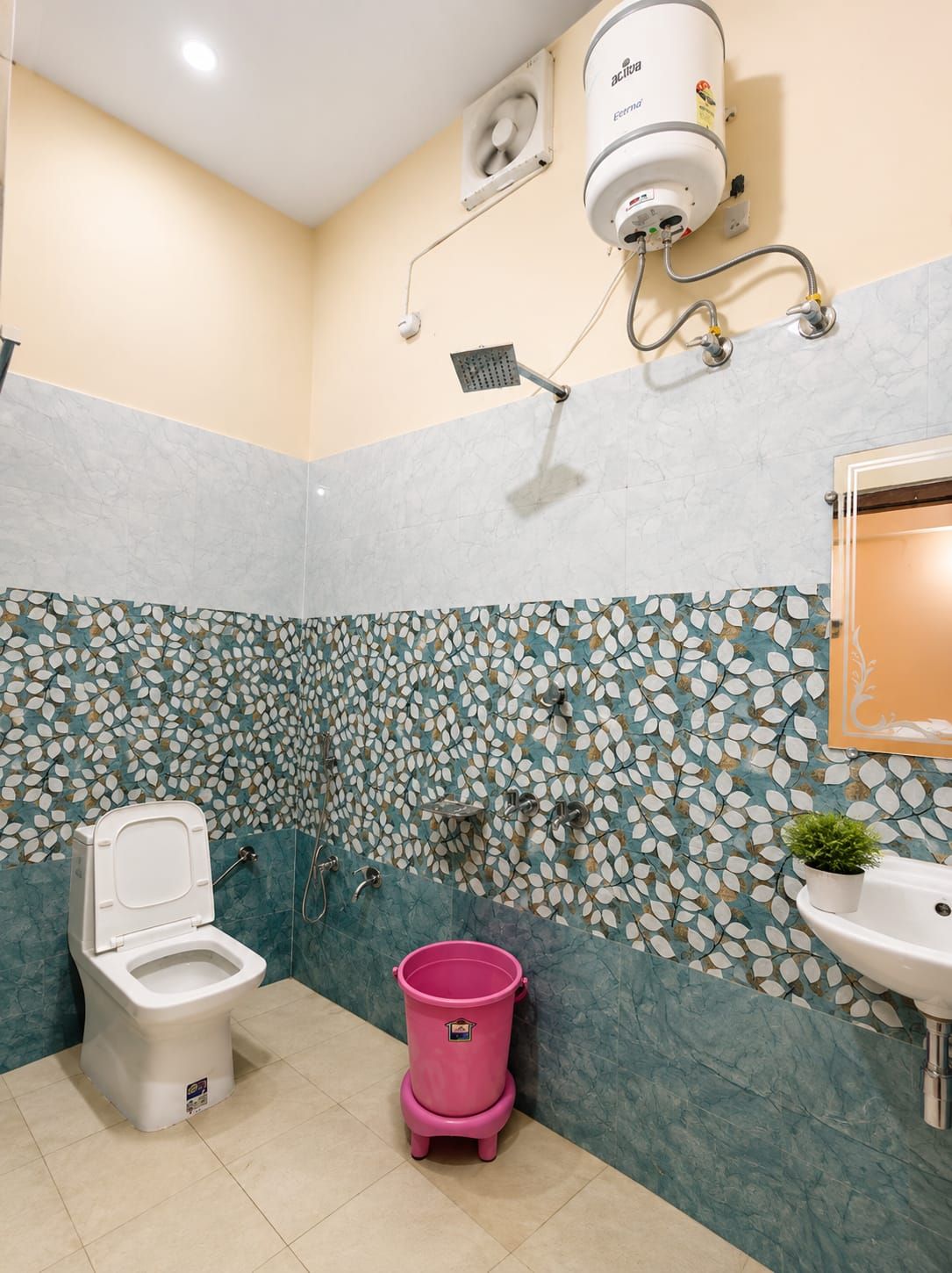 A bathroom with a toilet, a pink bucket, a showerhead, and a wall-mounted air purifier.