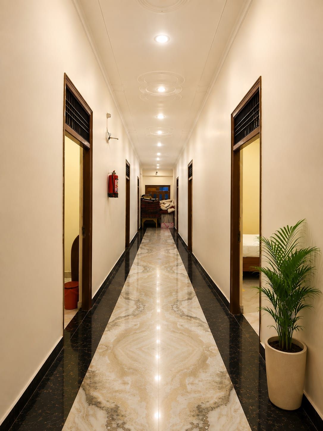 Un pasillo de hotel con piso de mármol, puertas a ambos lados y una planta en maceta a la derecha.