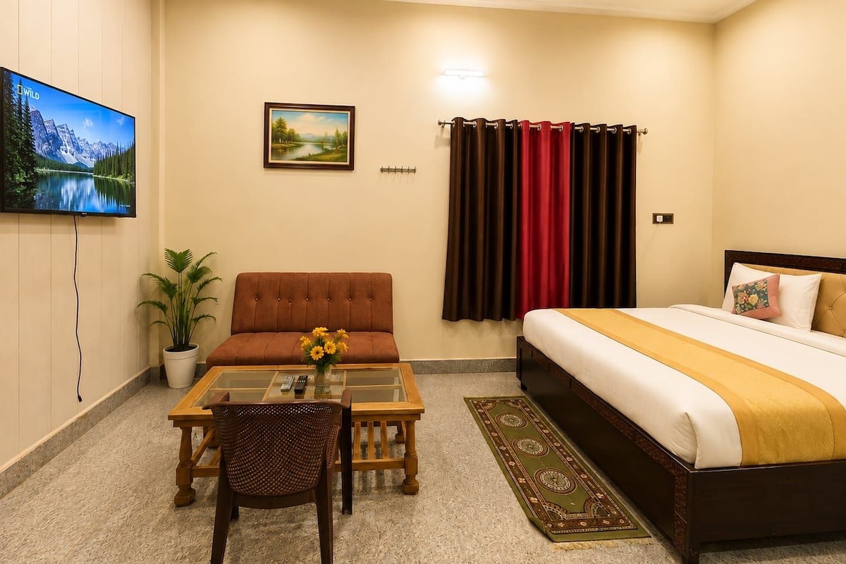 A hotel room with a bed, a sofa, a TV, a painting, and a window with curtains.