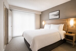 Ein Hotelzimmer mit einem großen Bett, einem Nachttisch, einer Wandleuchte und einem Fenster mit Jalousien.