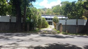 Una carretera pavimentada que conduce a un edificio con cerca blanca y árboles a ambos lados.