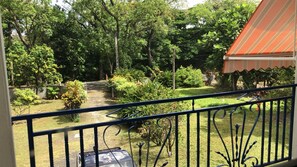 Un balcon donnant sur un jardin et un bâtiment doté d’une marquise à rayures.
