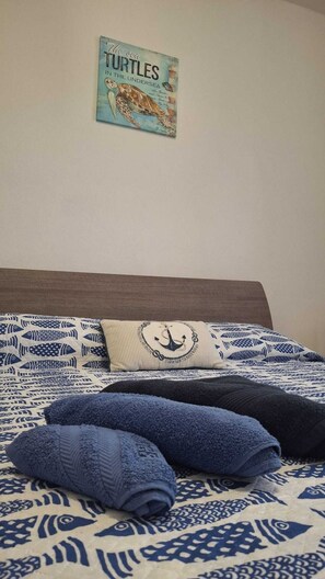 A bed with a patterned blue and white bedding, a pillow with an anchor design, and a wall-mounted sign with a turtle illustration. - L'Arèna Casa Vacanze elegante vicino al mare (Alghero)
