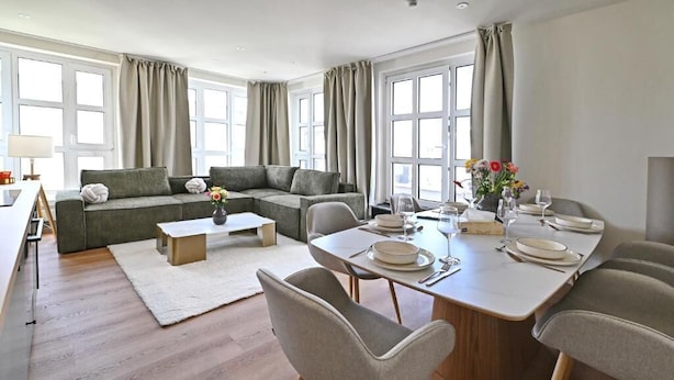 Una sala de estar moderna con sofá, mesa de centro y comedor con sillas y mesa lista para una comida.