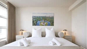 Una habitación de hotel con una cama grande, dos mesitas de noche, un cuadro en la pared y una ventana con cortinas.