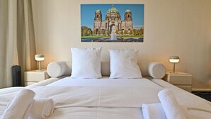 Una habitación de hotel con una cama grande, dos lámparas de noche y un cuadro de un edificio en la pared.