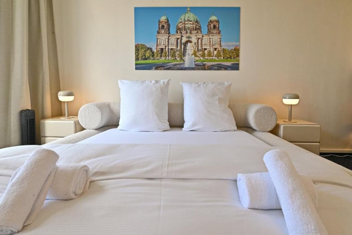 Una camera d'albergo con un letto grande, due lampade ai lati e un quadro raffigurante un edificio sulla parete.