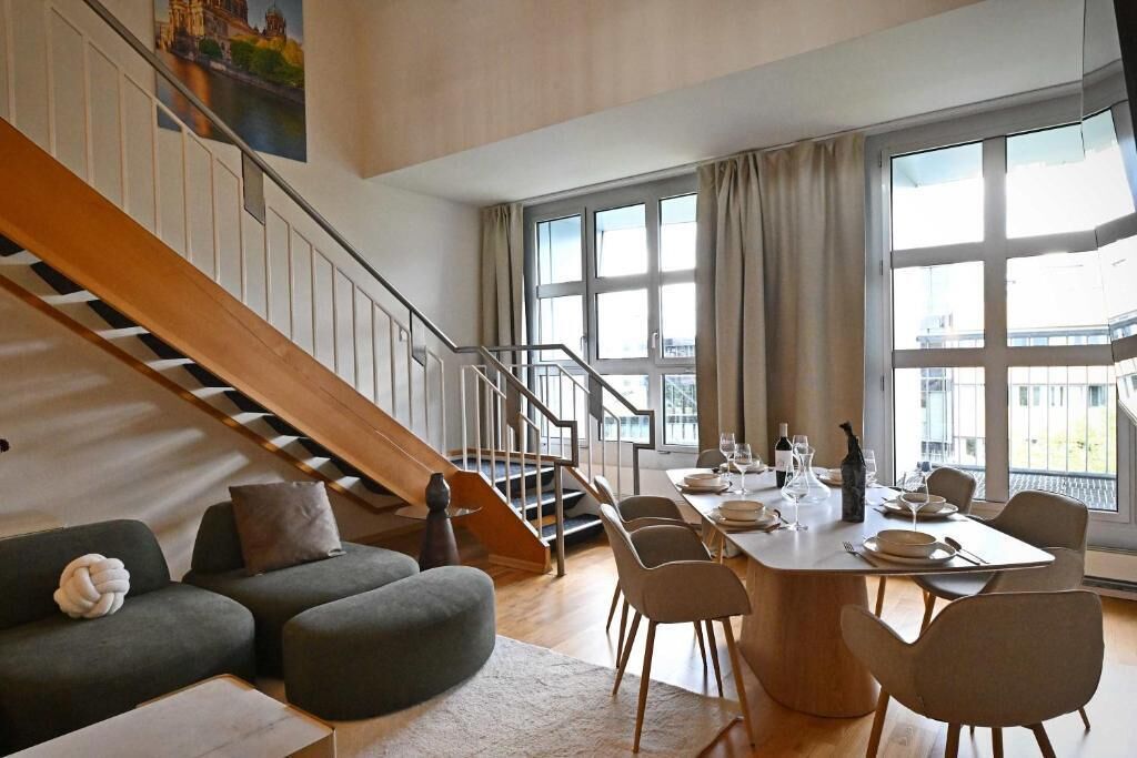 Un interior moderno con una escalera, un comedor y ventanas amplias.