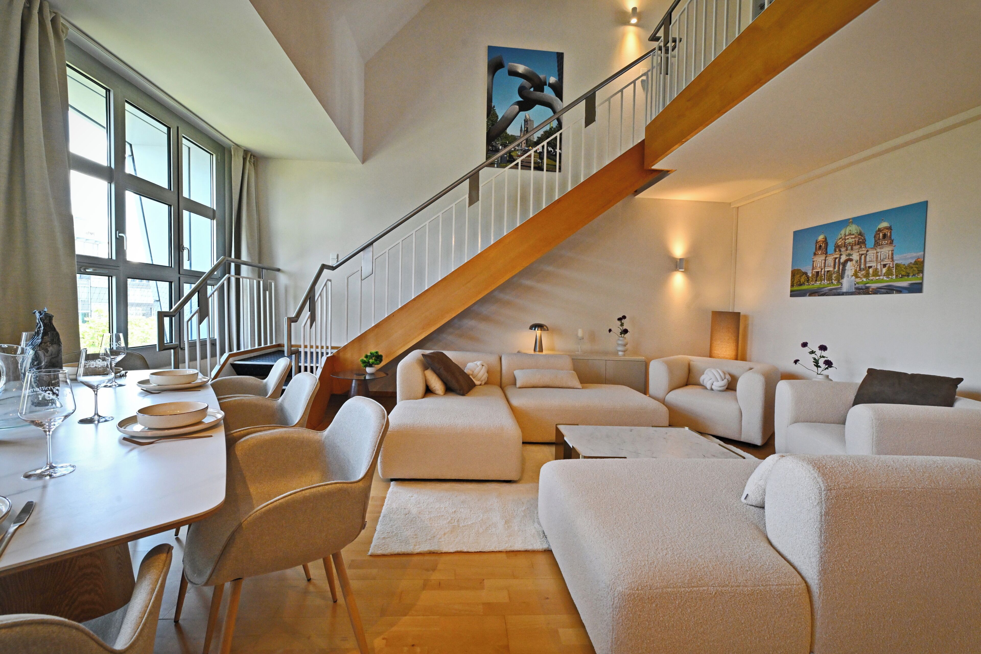 Ein geräumiger Wohnbereich mit Treppe, einem Esstisch mit Tellern und Gläsern sowie einer Couch.