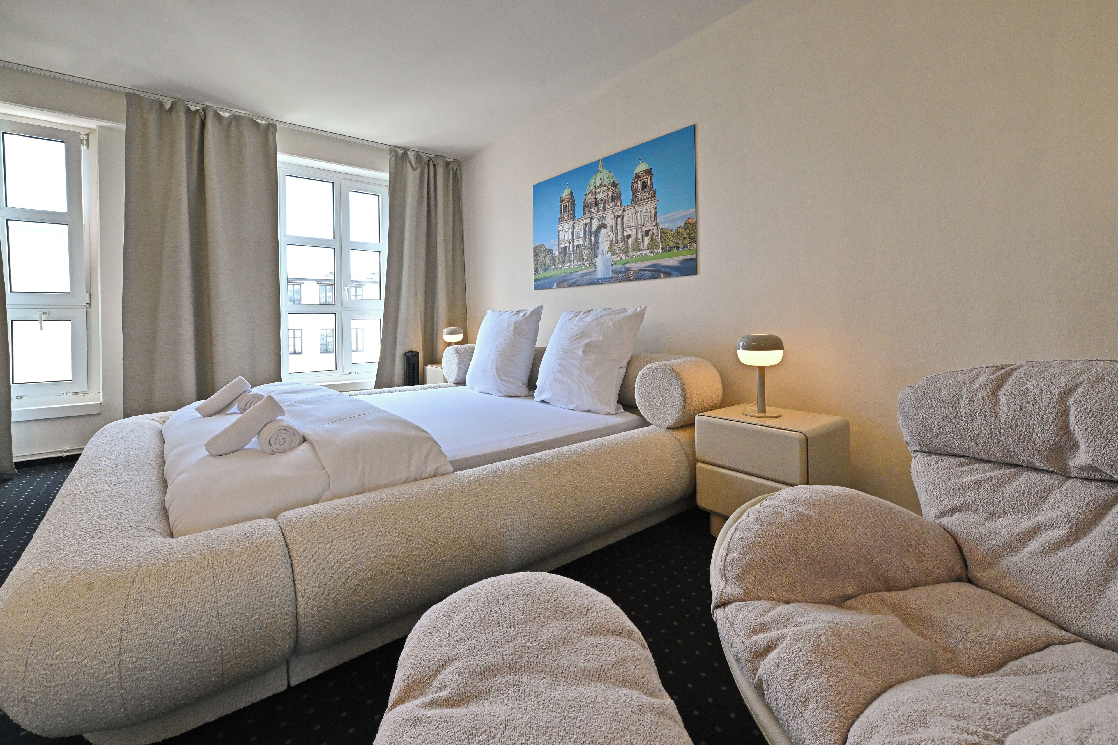 A hotel room with a large bed, two bedside tables, a nightstand, a chair, and a painting on the wall.