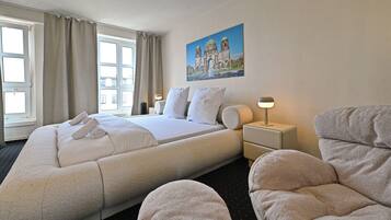 A hotel room with a large bed, two bedside tables, a nightstand, a chair, and a painting on the wall.