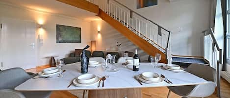 Un coin repas avec un escalier en bois, une table à manger dressée pour quatre personnes et un tableau accroché au mur.