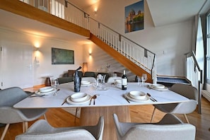 Uma área de jantar com escada de madeira, mesa posta para quatro pessoas e um quadro na parede.