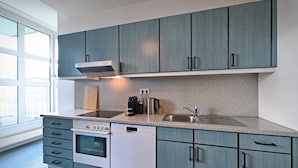 Una cocina moderna con armarios grises, horno empotrado, lavavajillas y cafetera.