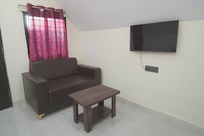 Een woonkamer met een bank, een salontafel, een aan de muur bevestigde televisie en een raam met gordijnen.