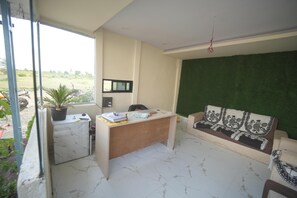 A room with a desk, a sofa, a potted plant, and a view of the outdoors.