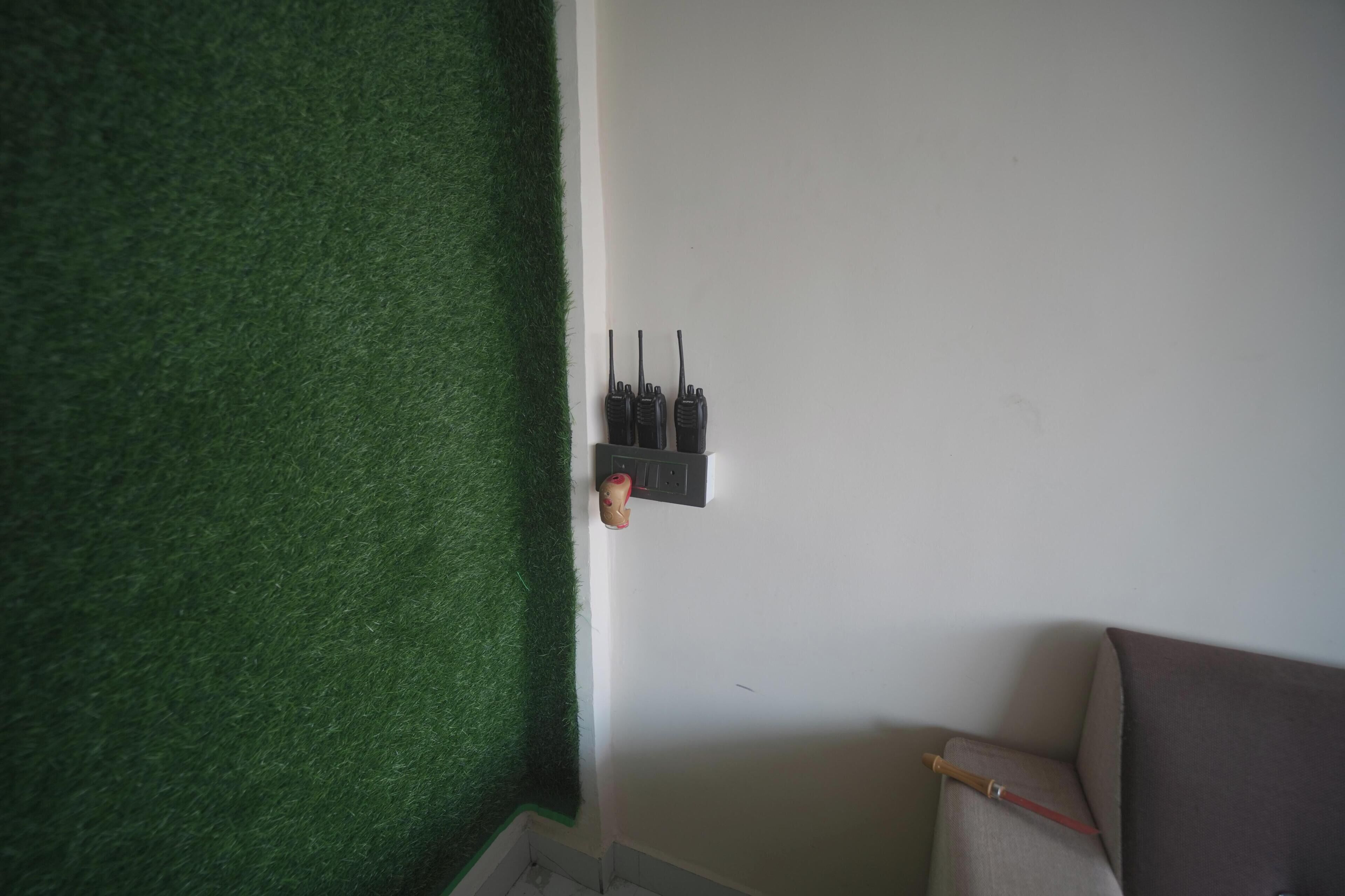 A room with a green artificial grass wall, a white wall with a mounted radio, and a brown chair.