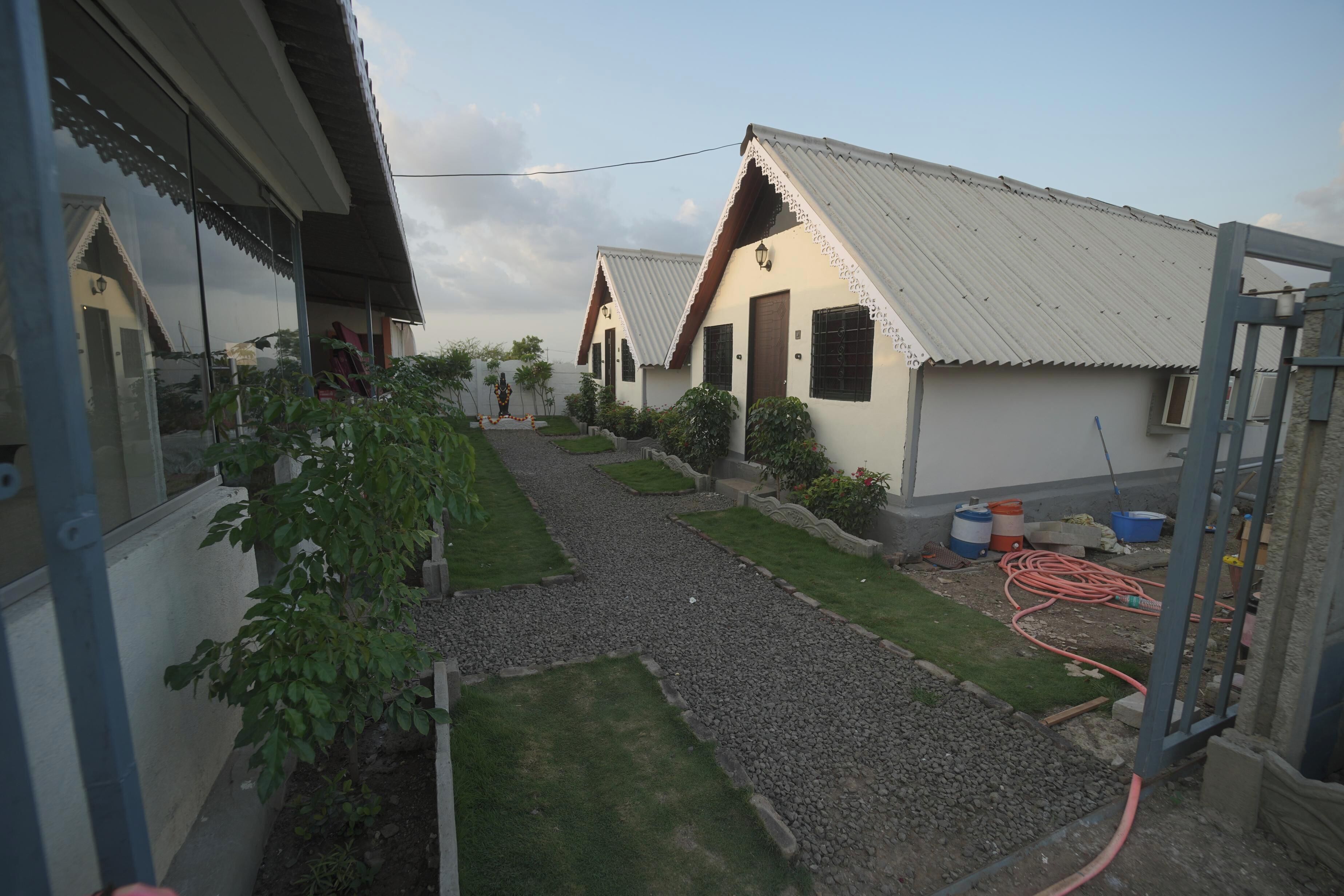 A courtyard with a gravel path, surrounded by buildings with corrugated metal roofs and a statue in the center.