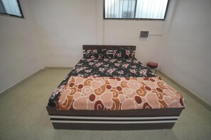 A bedroom with a bed, a window, and a small bedside table. - Shree Apex Resort (Pandharpur)