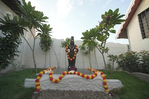 A statue with garlands, surrounded by greenery and a white wall. - Shree Apex Resort (Pandharpur)
