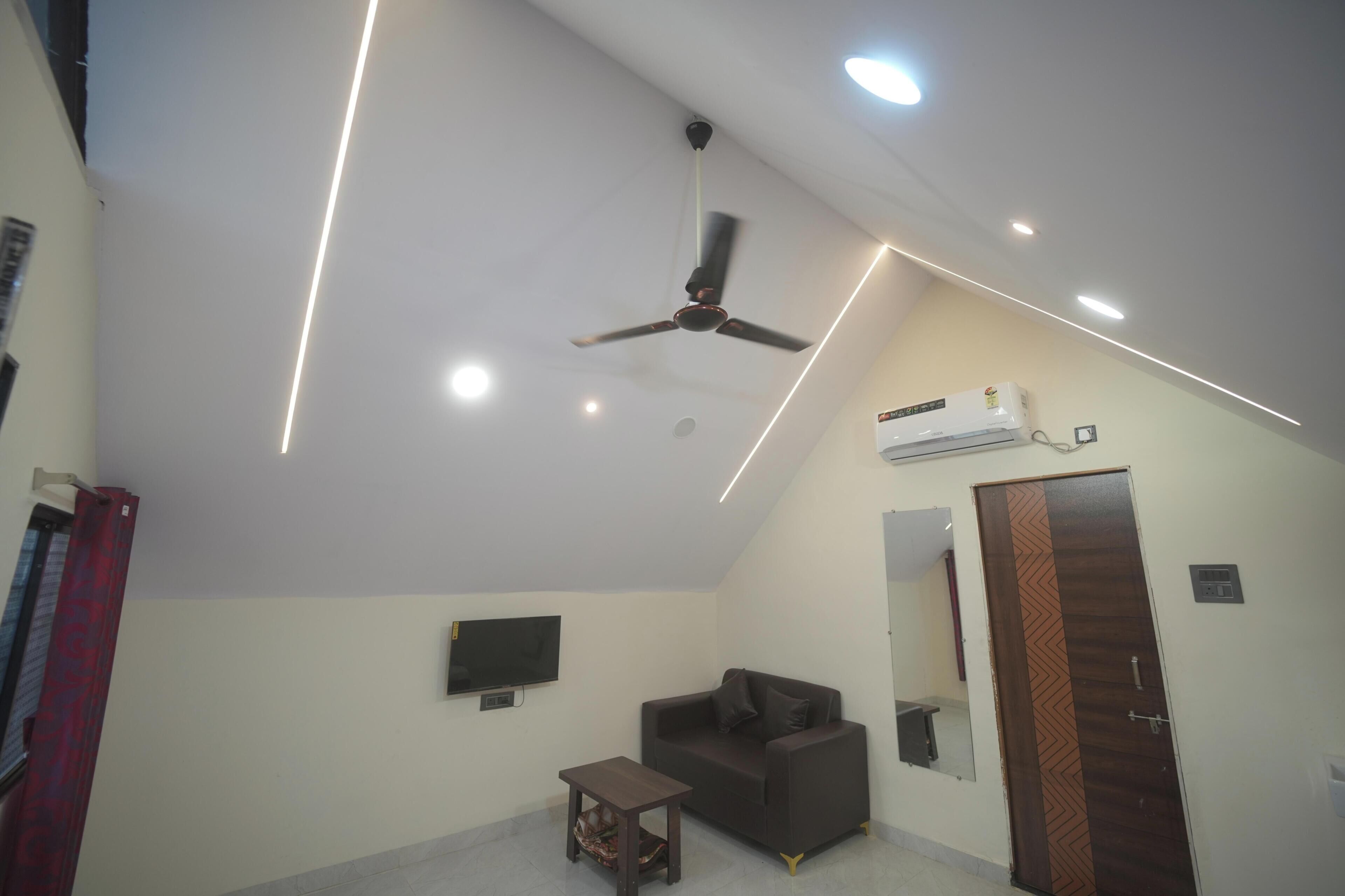 Una habitación con ventilador de techo, iluminación empotrada, televisor de pantalla plana, sofá, una mesita y un equipo de aire acondicionado.