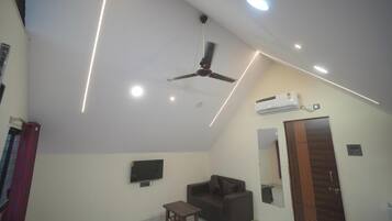 Una habitación con ventilador de techo, iluminación empotrada, televisor de pantalla plana, sofá, una mesita y un equipo de aire acondicionado.