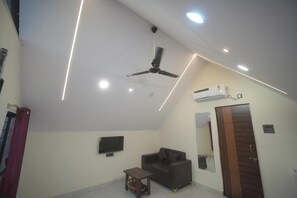 A room with a ceiling fan, recessed lighting, a flat-screen TV, a sofa, a small table, and an air conditioning unit.