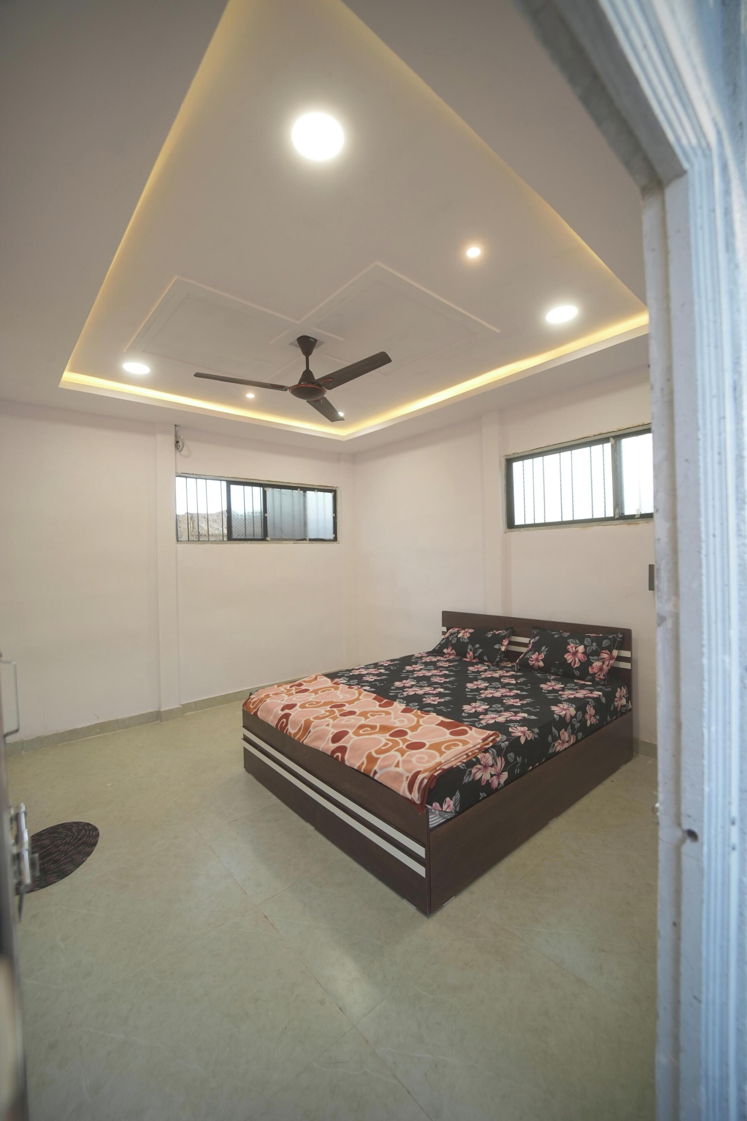 Quarto com cama, ventoinha no teto, iluminação embutida e janelas.