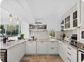 Une cuisine avec des meubles blancs, un îlot central et une vue sur une piscine.