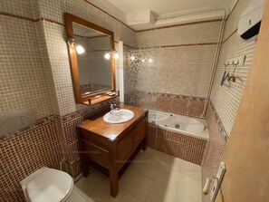 Ein Badezimmer mit einem Holzbadschrank, einem weißen Waschbecken, einem Spiegel und einer Badewanne.
