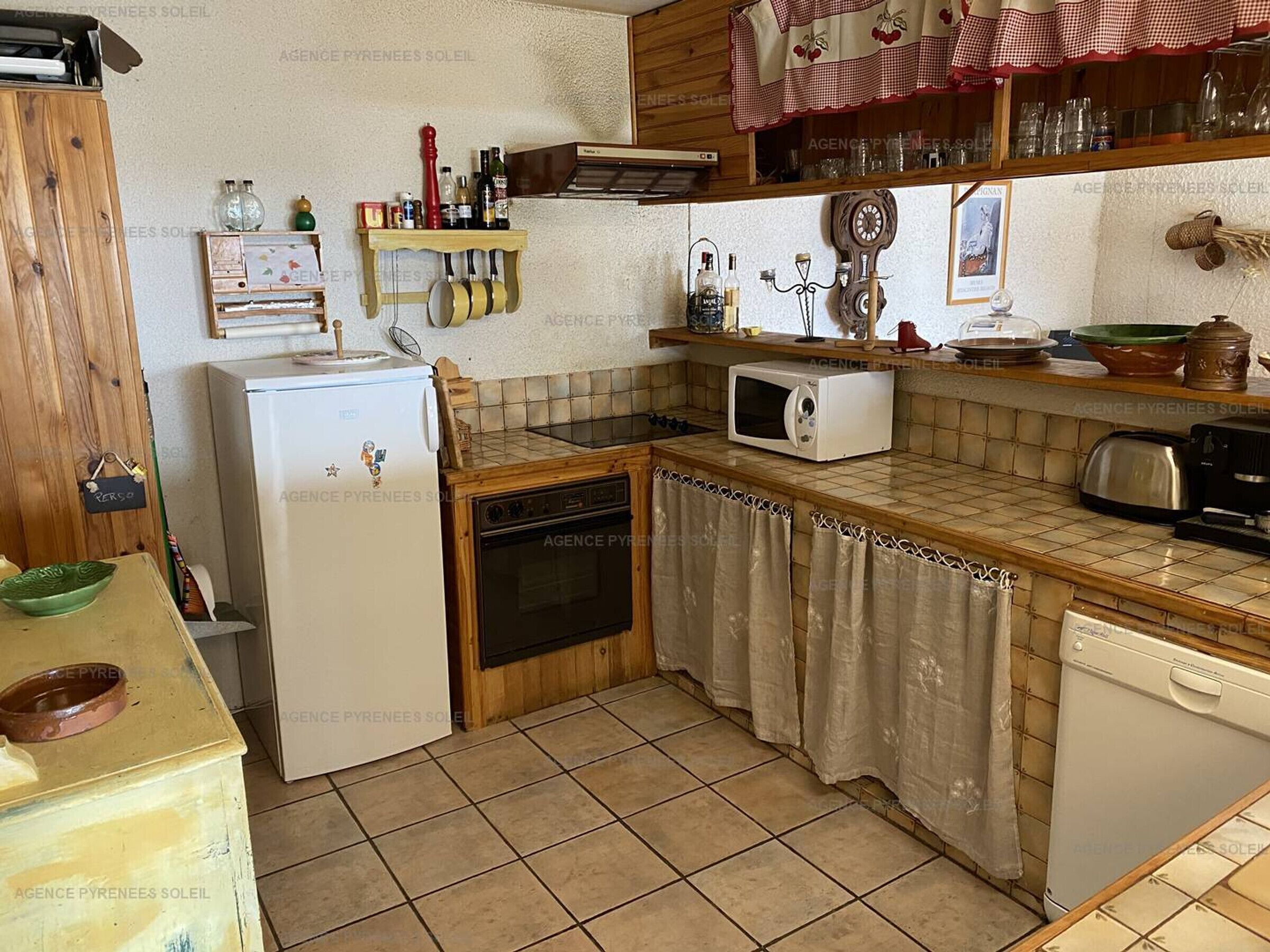 Eine kompakte Küche mit Kühlschrank, Mikrowelle, Backofen und Spüle. Holzschränke und eine geflieste Spritzschutzwand.