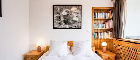 Quarto com teto de madeira, cama com roupa de cama branca, estante e quadro na parede.