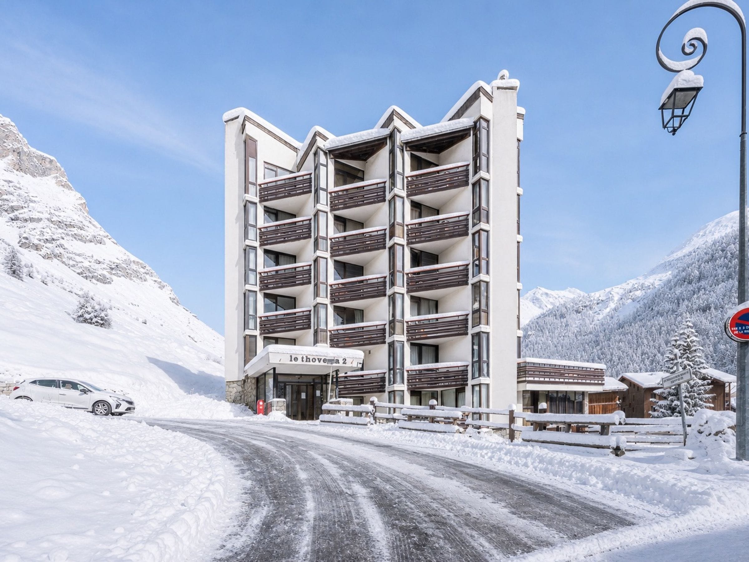 A multi-story hotel with balconies, a snow-covered mountain backdrop, and a clear sky.