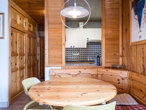 A wooden interior with a round table and chairs, a hanging light fixture, and a kitchen area in the background. - Bright apartment village view - 6 guests (Val-d'Isère)