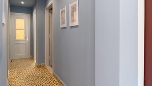 A hallway with a patterned floor, a white door, and two framed artworks on the wall.