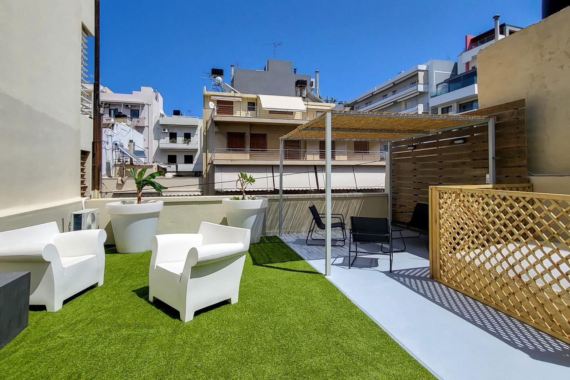 A rooftop terrace with artificial grass, white lounge chairs, and a wooden pergola.