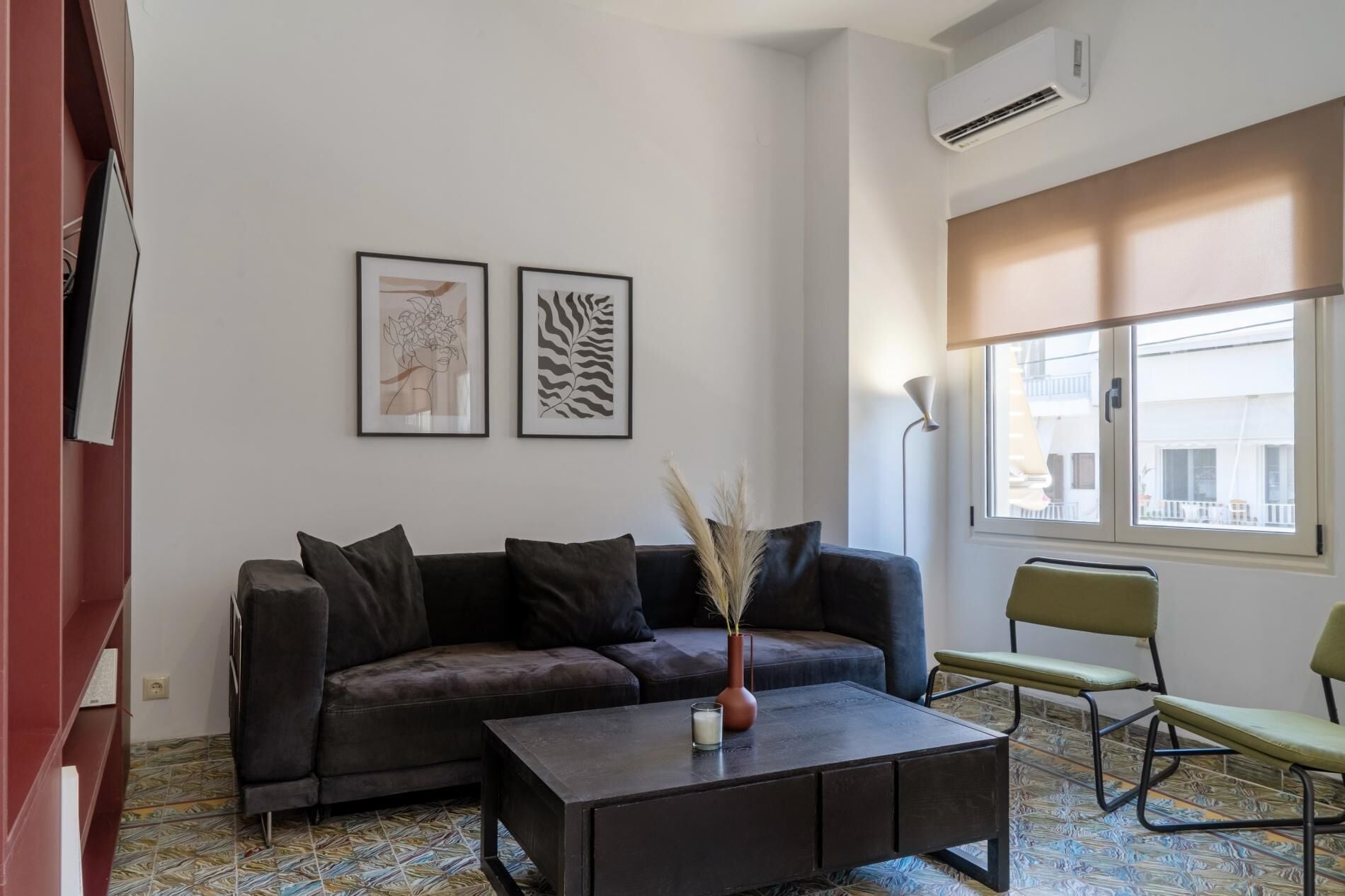 A modern living room with a sofa, a coffee table, and a chair. There are two framed artworks on the wall, and an air conditioning unit is mounted on the wall.